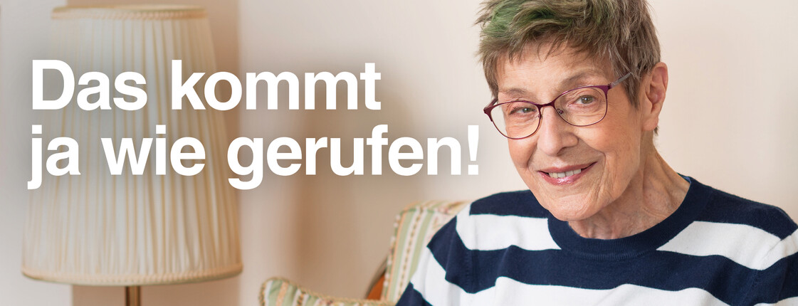 Ältere Frau mit kurzen grau-grünen Haaren und Brille sitzt lächelnd im Sessel, liest Zeitung und trägt ein Notrufarmband am Handgelenk