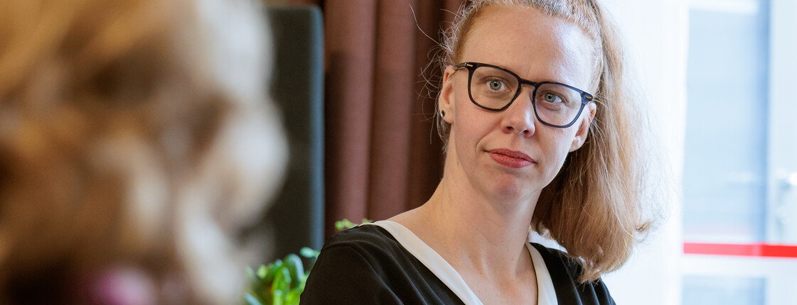 Eine Caritas Mitarbeiterin, die einer pflegenden Angehörigen gegenüber sitzt, hört aufmerksam zu.