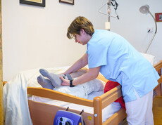 Pflegekraft unterstützt Bewohner*in beim Anziehen der Socken im Pflegebett.