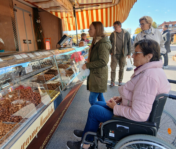 Gruppe von Menschen, einige in Rollstühlen, an einem Marktstand mit Nüssen und Süßigkeiten.