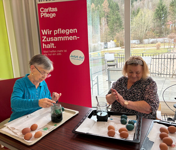 Zwei Bewohner*innen färben Ostereier an einem Tisch im Pflegewohnhaus.