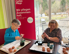Zwei Bewohner*innen färben Ostereier an einem Tisch im Pflegewohnhaus.