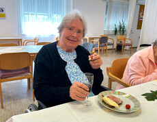 Bewohnerin sitzt mit Wein und Jause an einem festlich gedeckten Tisch.