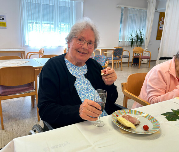 Bewohnerin sitzt mit Wein und Jause an einem festlich gedeckten Tisch.