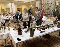 Tische mit handgefertigter Osterdekoration bei einem Basar im Innenbereich eines Pflegewohnhauses, mehrere Personen betrachten die Ausstellungsstücke