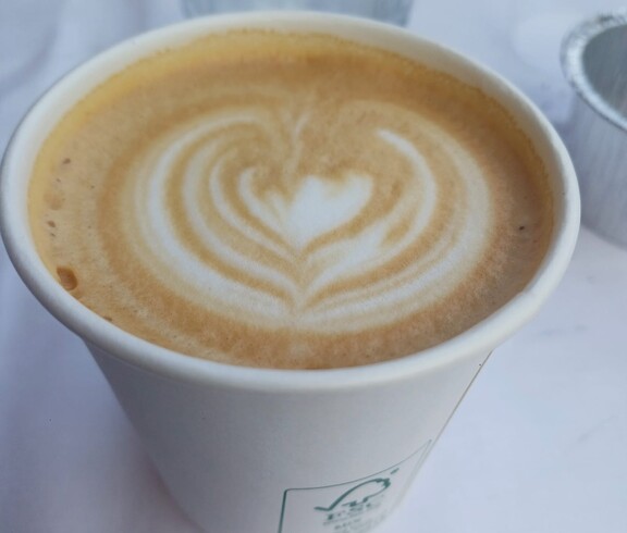 Ein Becher Kaffee mit herzförmigem Milchschaummuster steht auf einem weiß gedeckten Tisch und wurde beim Sommerfest als süße Begleitung zu Waffeln serviert.