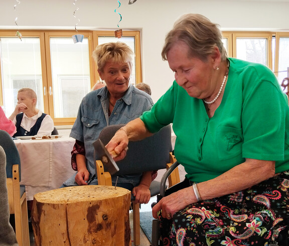 Bewohnerin schlägt mit Hammer im Spiel „Triff den Nagel“ einen Nagel in einen Holzblock ein.