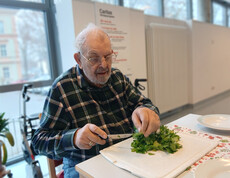 Ein Senior schneidet frische Kräuter an einem Tisch im Aufenthaltsraum.