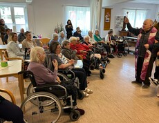 Geistlicher weiht die mitgebrachten Speisen vor sitzenden Bewohner*innen im Gemeinschaftsraum.