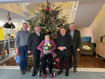 Hausleiter Josef Url, Bürgermeister ÖkR Josef Niggas, Vizebürgermeister Robert Sauer und BPO 2. Landtagspräsident Werner Amon, MBA, stehen nebeneinander und posieren für ein Gruppenfoto. In der Mitte steht Frau Markl, die einen Blumenstrauß in den Händen hält. Hinter der Gruppe ist ein festlich geschmückter Christbaum zu sehen. Die Personen blicken freundlich in die Kamera und stehen in einem offiziellen oder feierlichen Rahmen zusammen. 