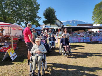 Senior*innen im Rollstuhl vor bunten Marktständen, Berge im Hintergrund