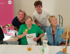 Seniorin mit Urkunde und Pokal, umgeben von Mitfeiernden und Mitarbeitenden der Caritas.