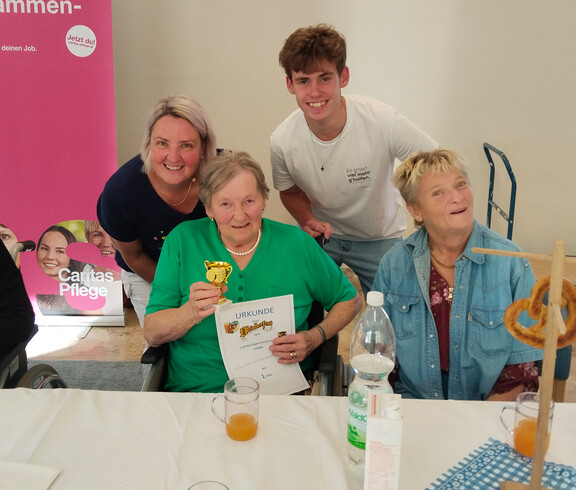 Seniorin mit Urkunde und Pokal, umgeben von Mitfeiernden und Mitarbeitenden der Caritas.