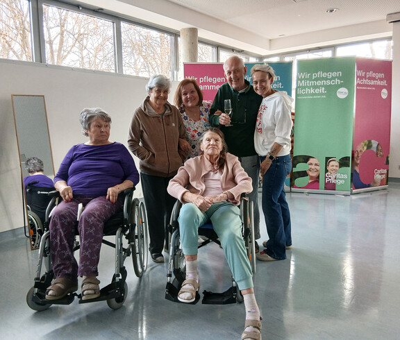 Bewohner*innen posieren gemeinsam vor Info‑Wänden der Caritas Pflege