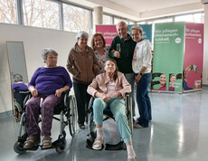 Bewohner*innen posieren gemeinsam vor Info‑Wänden der Caritas Pflege