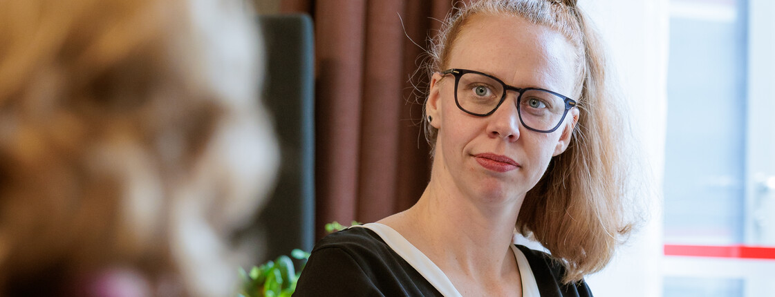 Eine Caritas Mitarbeiterin, die einer pflegenden Angehörigen gegenüber sitzt, hört aufmerksam zu.