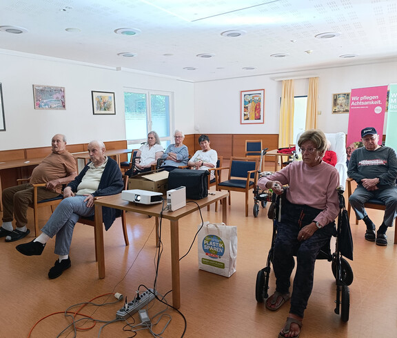 Bewohner*in mit Rollator hält Wii-Controller und nimmt am virtuellen Bowling in Haus Anna teil.