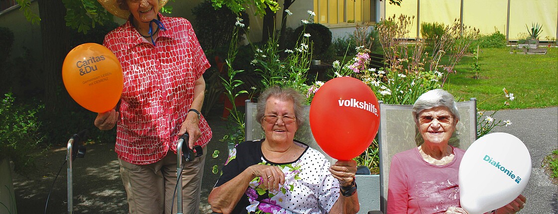 Drei ältere Frauen sind im Freien und halten einen Luftballon hoch.