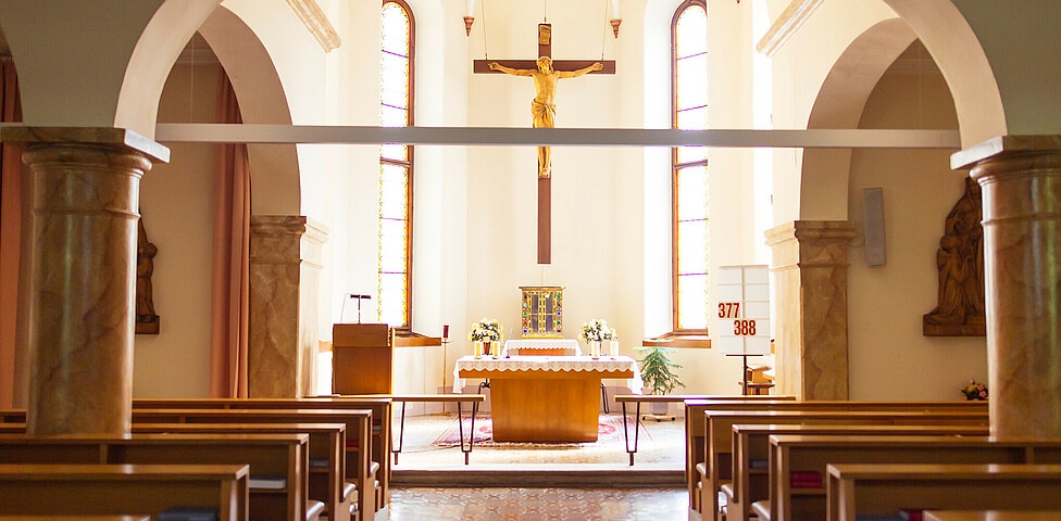 Die Kappele mit Kirchenbänken rechts und links, sowie den Altar in der Mitte. Über diesem hängt ein großes Kreuz.