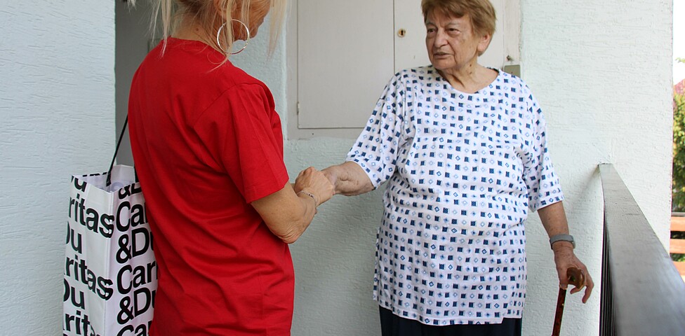 Caritas Mitarbeiterin der Hauskrankenpflege begrüßt Klientin zuhause