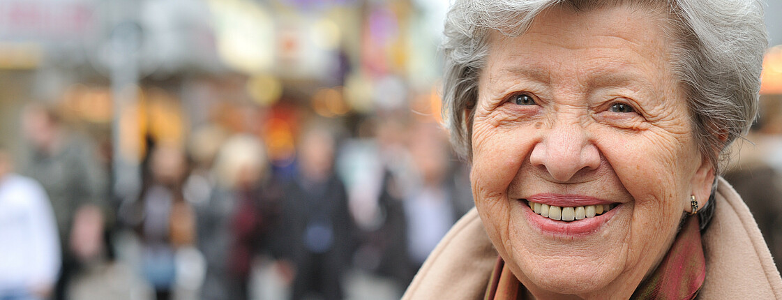 Portrait einer Seniorin in einer Fußgängerzone.