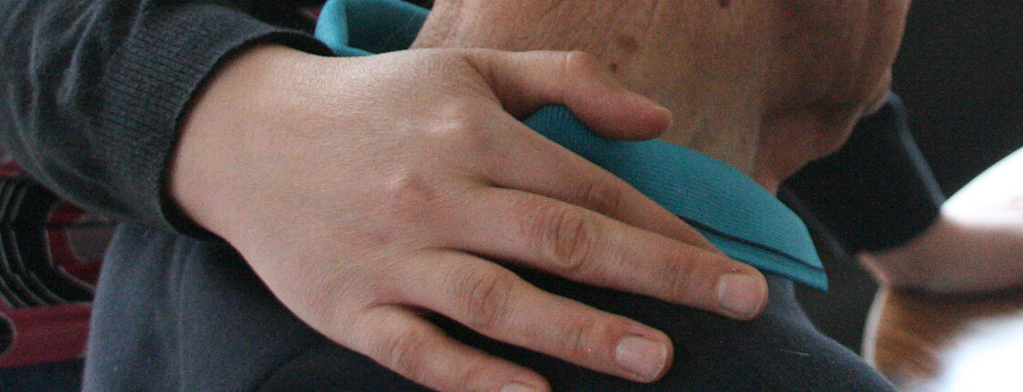 Eine junge Hand liegt auf den Schultern eines älteren Mannes.