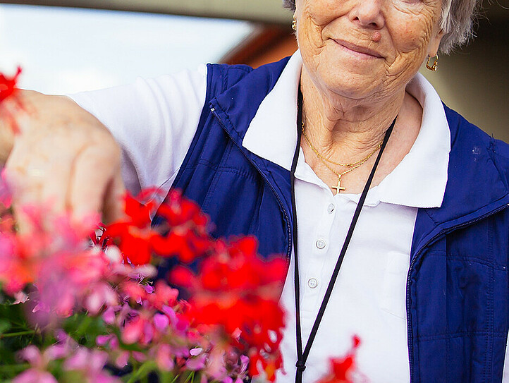 Eine ältere Dame kümmert sich um die Balkonblumen auf der Terasse.