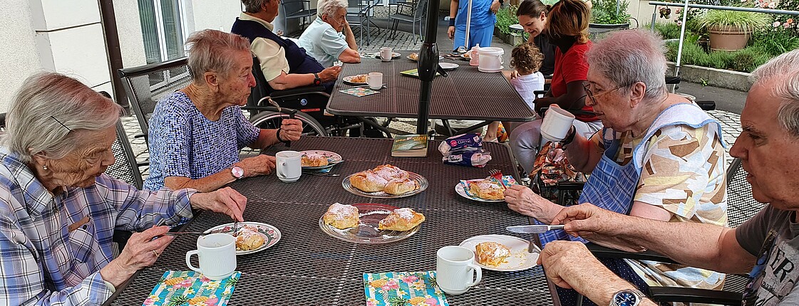 Mehrere Senior*innen sitzen am Tisch im Garten bei Kaffee und Kuchen