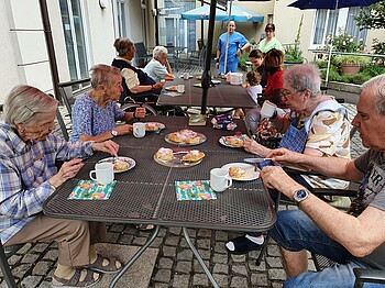 Mehrere Senior*innen sitzen am Tisch im Garten bei Kaffee und Kuchen