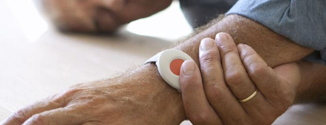 Eine Hand betätigt den Knopf des Notrufbandes am Arm