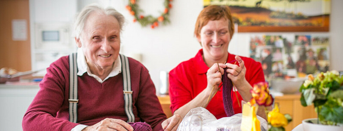 Ein alter Mann und eine ältere Frau sitzen am Tisch und stricken. 