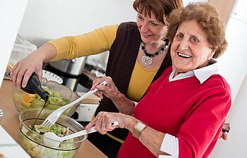 Zwei Frauen machen Salat und lachen.