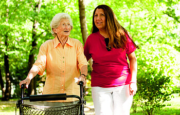 Eine Seniorin und eine Pflegerin spazieren durch den Wald.