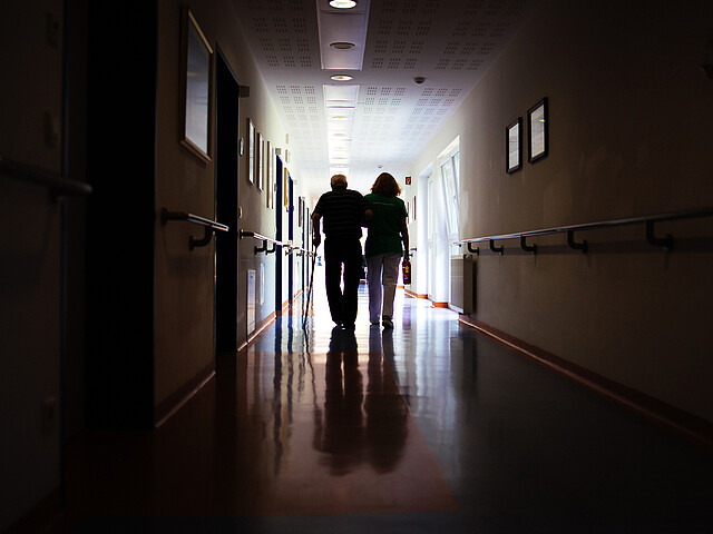 Zwei Personen gehen einen Gang entlang, man sieht nur ihre dunklen Silhouetten, da das Ziel hell beleuchtet ist.