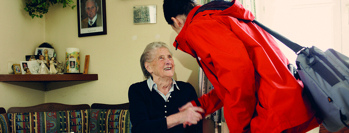 Eine Caritas Pflegerin begrüßt eine Klientin zuhause.