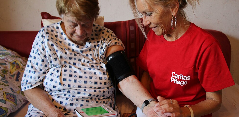 Caritas Mitarbeiterin der Hauskrankenpflege misst Blutdruck bei Klientin