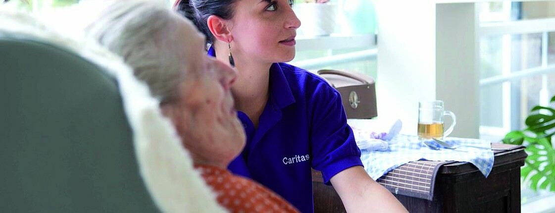 Eine Betreuerin der Caritas hält die Hand einer Seniorin